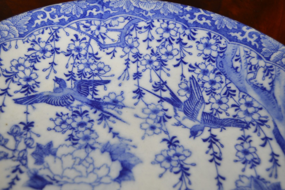 A circular blue and white porcelain charger decorated with hand-painted carp fish, birds, and floral foliage inside a geometric patterned border. View VI