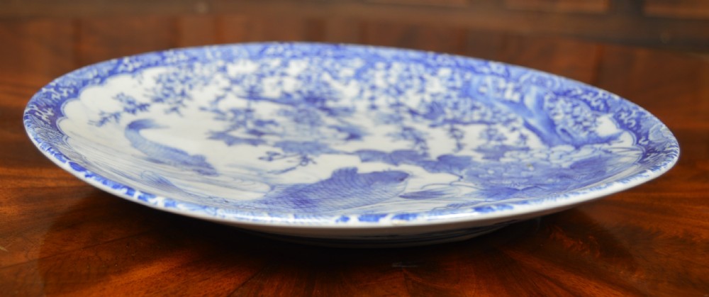 A circular blue and white porcelain charger decorated with hand-painted carp fish, birds, and floral foliage inside a geometric patterned border. View VIII