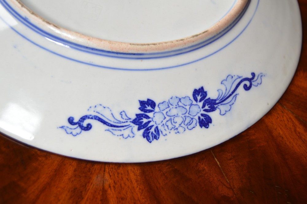 A circular blue and white porcelain charger decorated with hand-painted carp fish, birds, and floral foliage inside a geometric patterned border. View IX