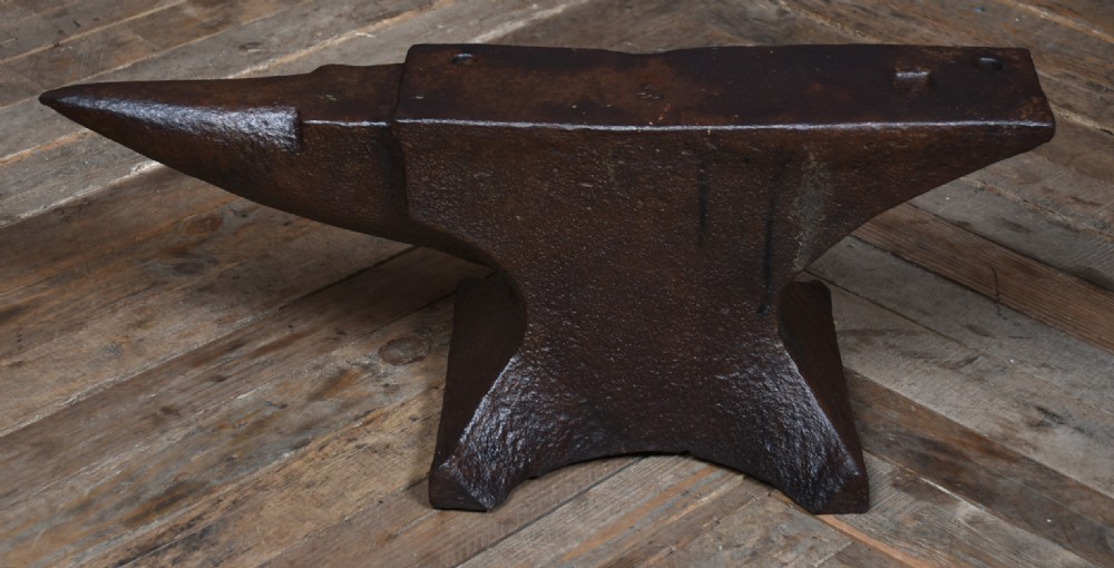 A dark brown cast iron blacksmith anvil featuring a flat face, conical horn, and square hardy hole resting on a wooden floor. View IV