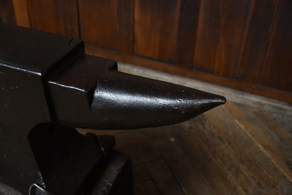 A heavy dark cast iron blacksmith anvil mounted on a weathered square timber block. View VII