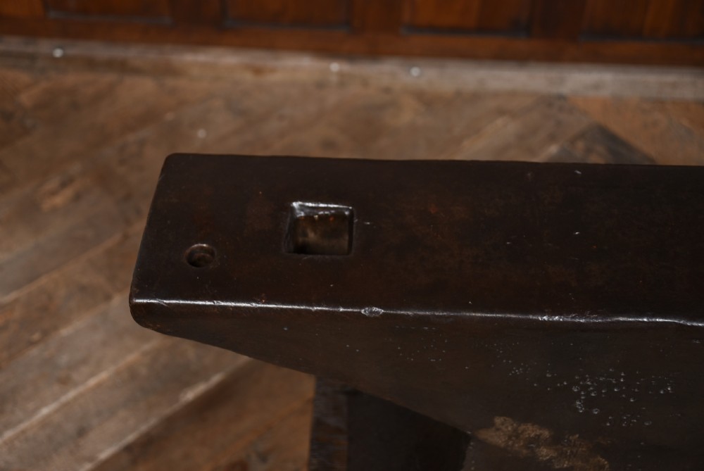 A heavy dark cast iron blacksmith anvil mounted on a weathered square timber block. View VIII
