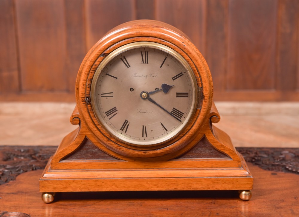 An antique oak mantel clock featuring a rounded arch case, brass dial with Roman numerals, marked Thwaites and Reed London, raised on brass bun feet.