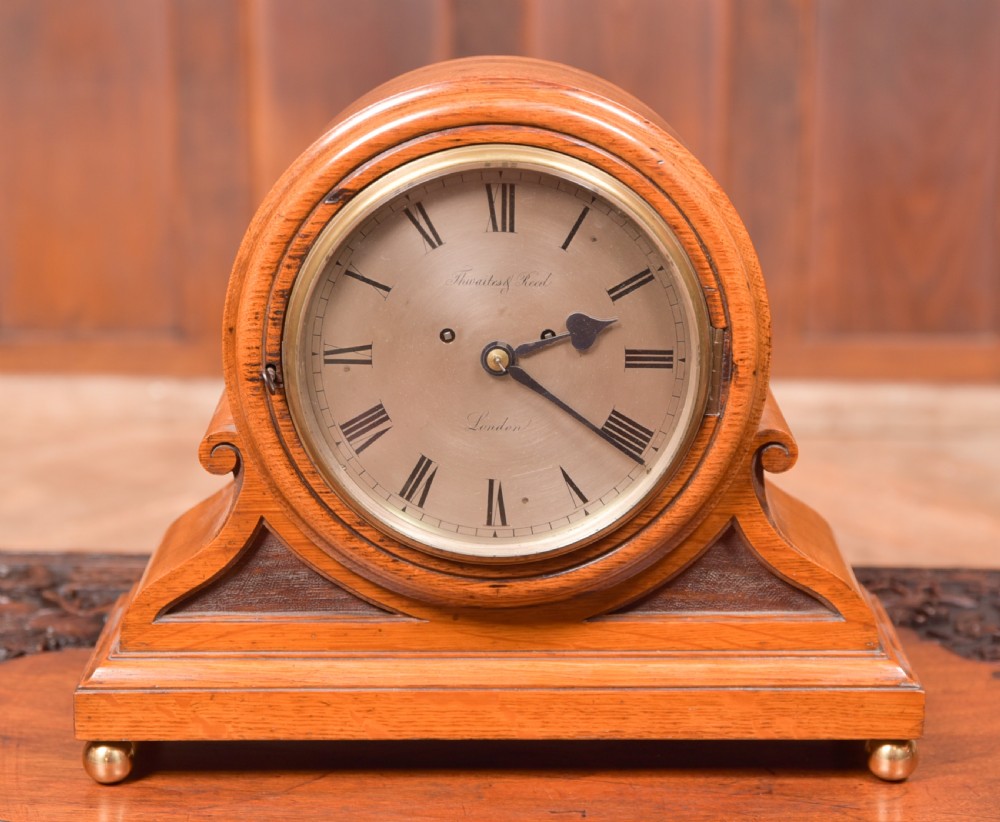 An antique oak mantel clock featuring a rounded arch case, brass dial with Roman numerals, marked Thwaites and Reed London, raised on brass bun feet. View II