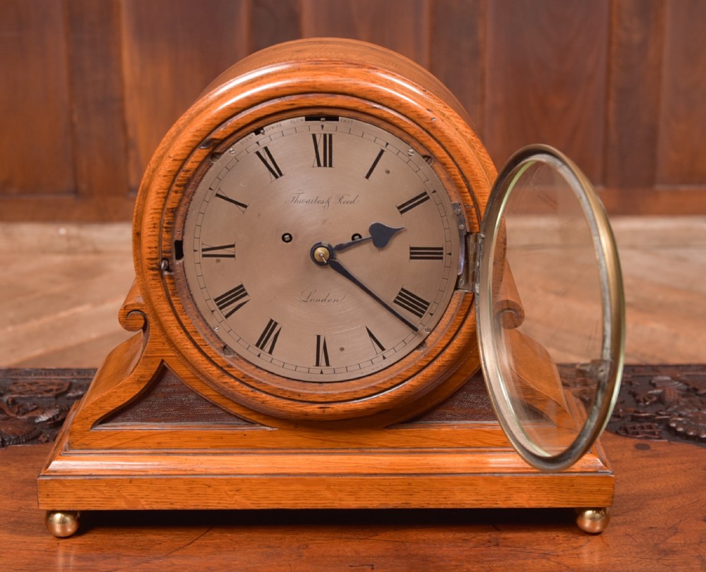 An antique oak mantel clock featuring a rounded arch case, brass dial with Roman numerals, marked Thwaites and Reed London, raised on brass bun feet. View VIII