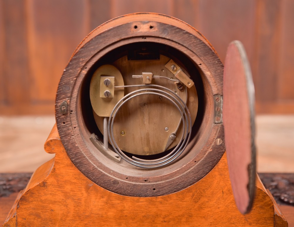 An antique oak mantel clock featuring a rounded arch case, brass dial with Roman numerals, marked Thwaites and Reed London, raised on brass bun feet. View XII