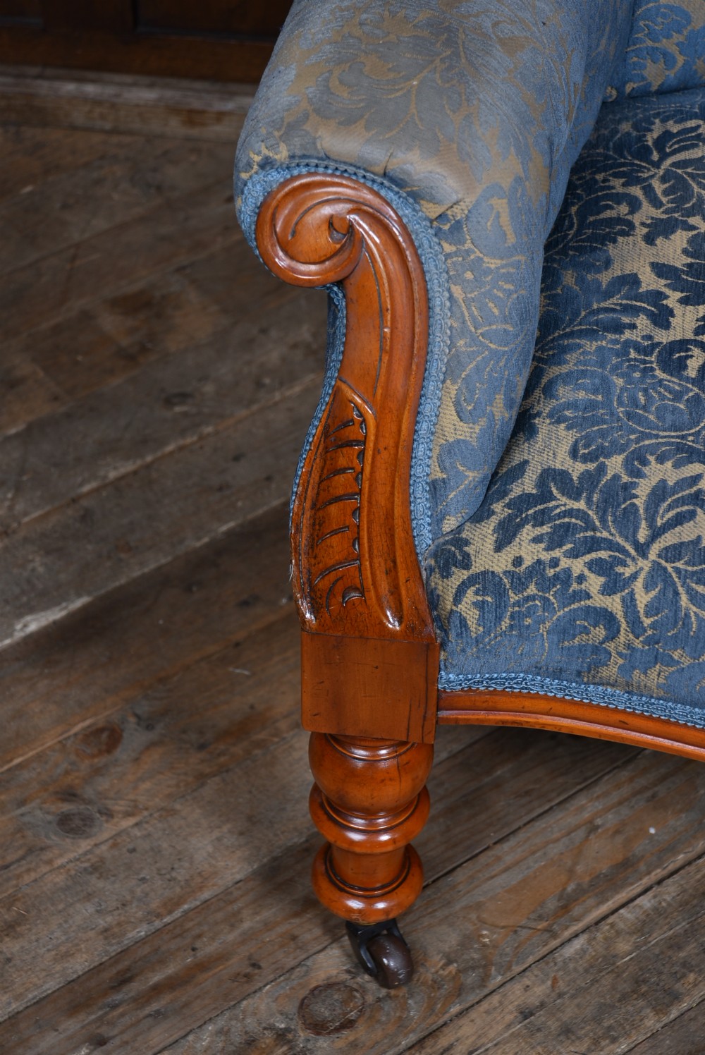 A Victorian mahogany armchair with a carved top cresting, deep buttoned blue patterned fabric upholstery, padded scroll arms, and turned front legs on brass castors. View VI