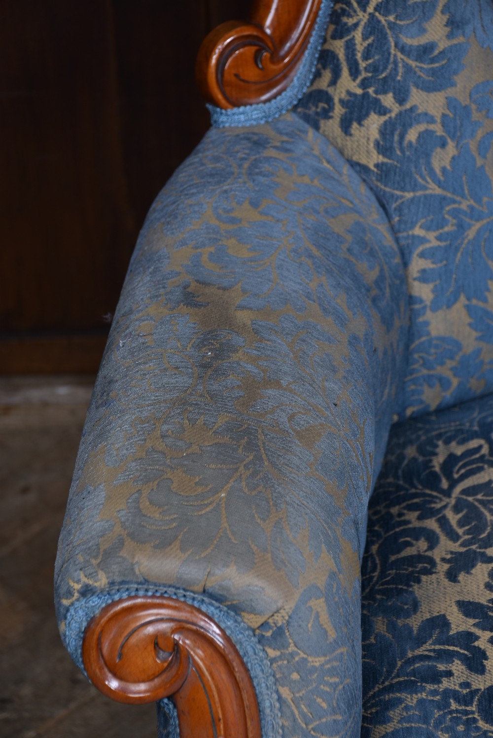 A Victorian mahogany armchair with a carved top cresting, deep buttoned blue patterned fabric upholstery, padded scroll arms, and turned front legs on brass castors. View VII