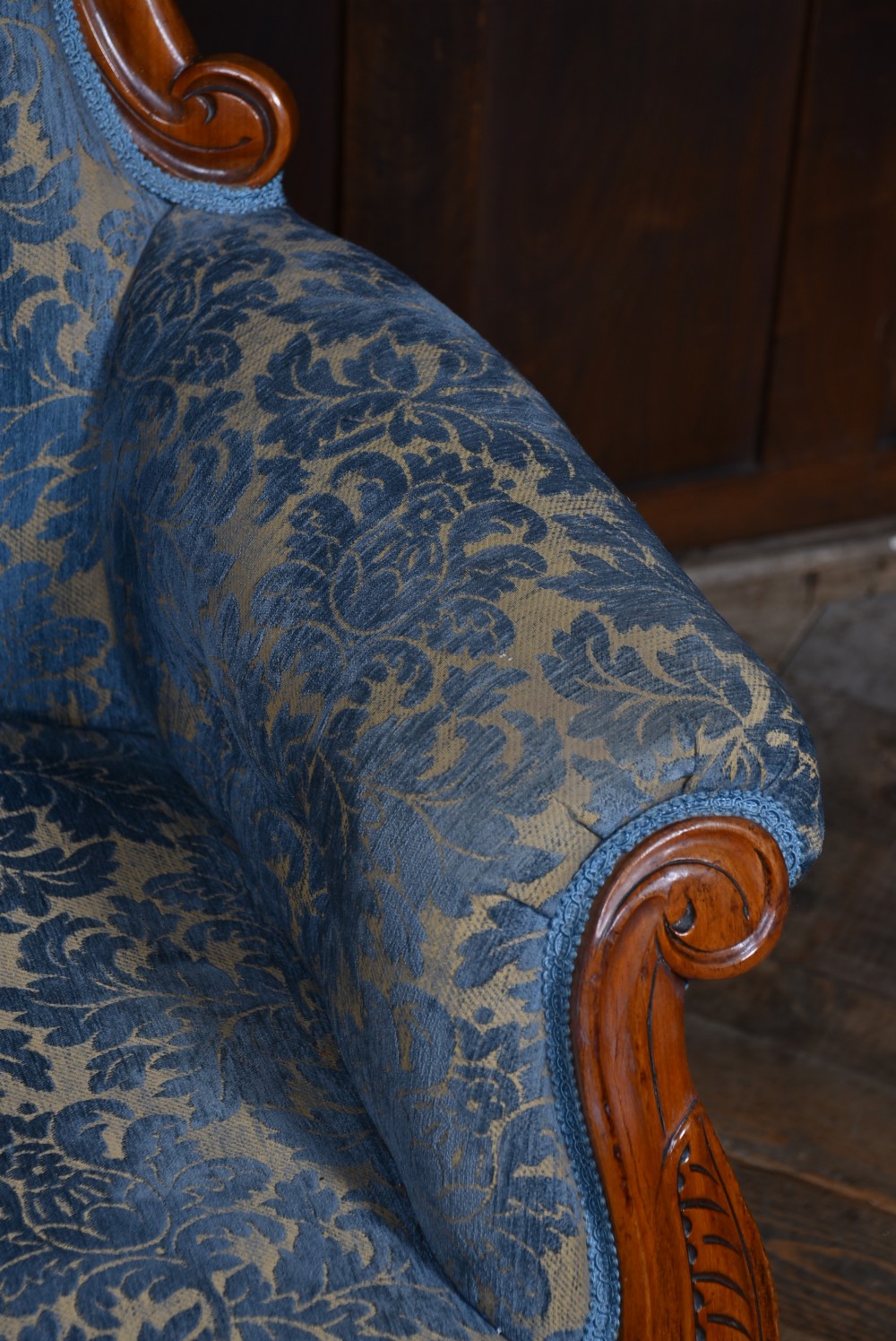 A Victorian mahogany armchair with a carved top cresting, deep buttoned blue patterned fabric upholstery, padded scroll arms, and turned front legs on brass castors. View VIII