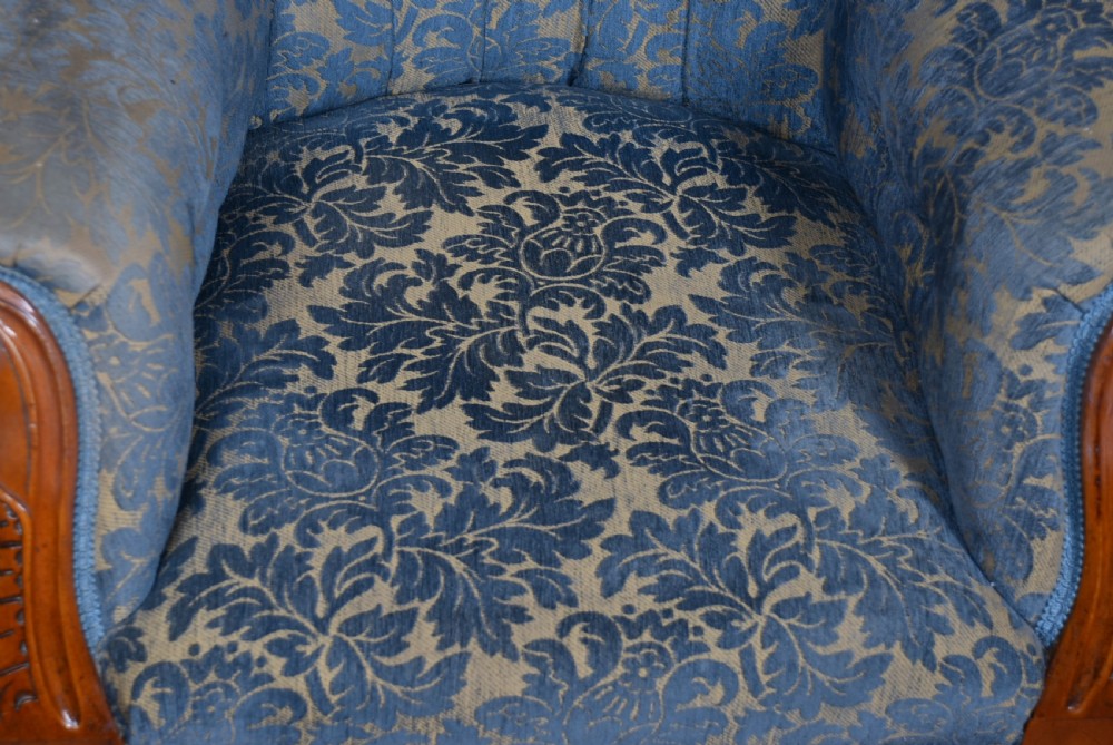 A Victorian mahogany armchair with a carved top cresting, deep buttoned blue patterned fabric upholstery, padded scroll arms, and turned front legs on brass castors. View IX