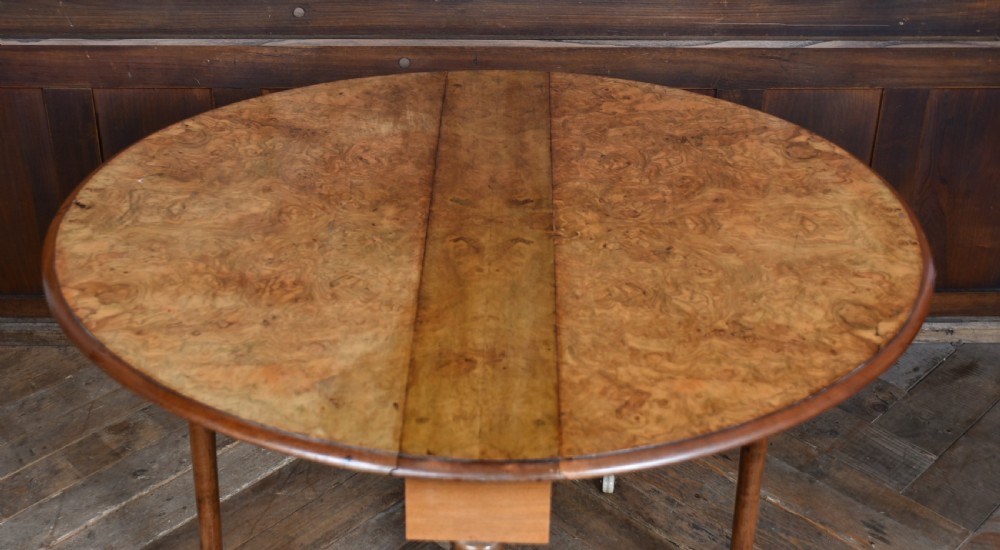 A Victorian burr walnut Sutherland table featuring hinged drop leaves, turned twin supports, carved cabriole feet, and white ceramic castors. View X