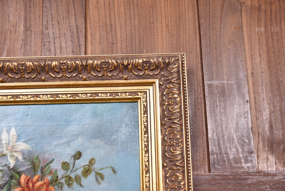 A framed oil painting depicting a floral arrangement in a classical urn resting on a stone pedestal against a blue sky. View VI