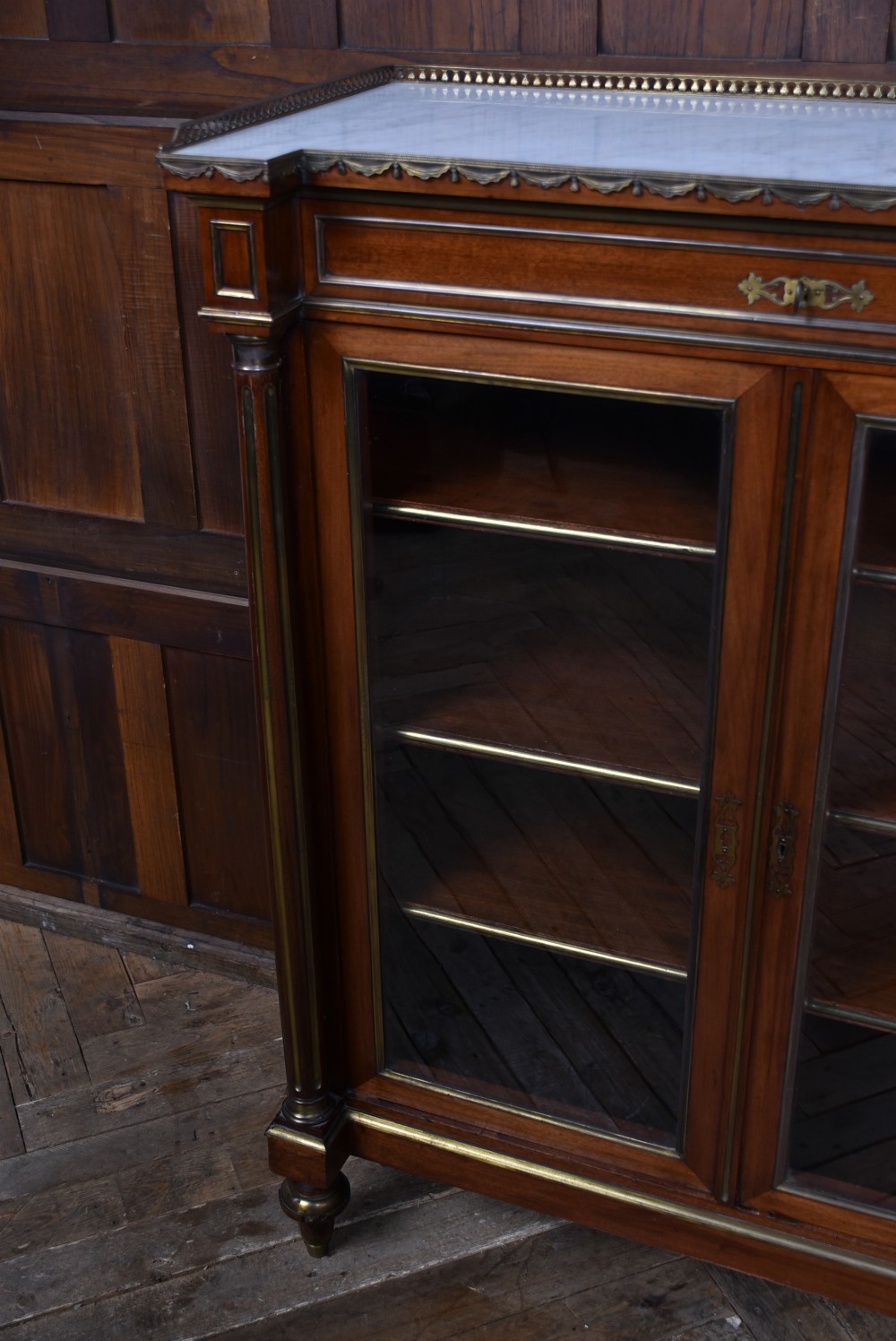 A French mahogany glazed bookcase featuring two glass-panelled doors, brass mounts, fluted side columns, and a light marble top. View VI