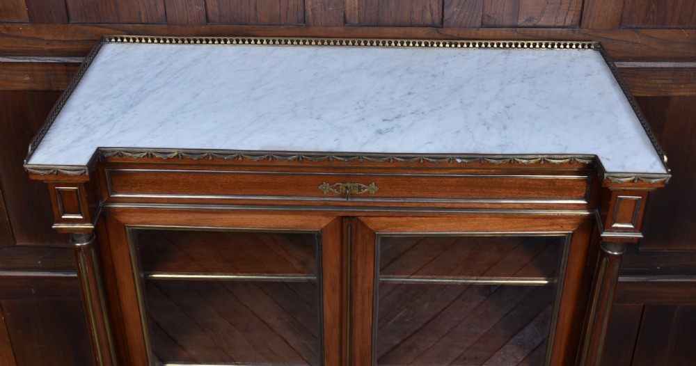A French mahogany glazed bookcase featuring two glass-panelled doors, brass mounts, fluted side columns, and a light marble top. View VIII