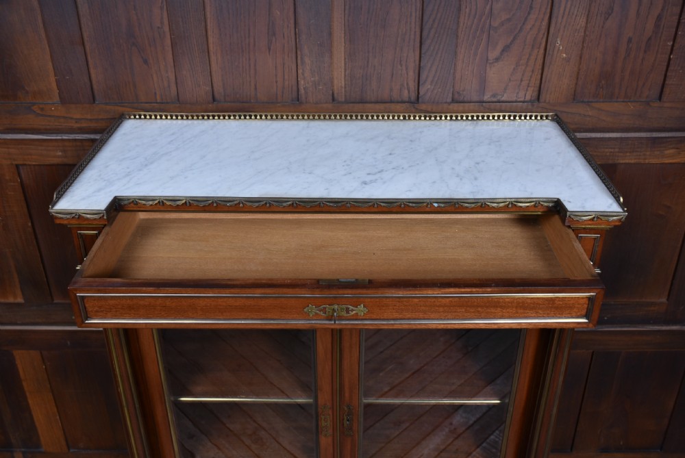 A French mahogany glazed bookcase featuring two glass-panelled doors, brass mounts, fluted side columns, and a light marble top. View IX