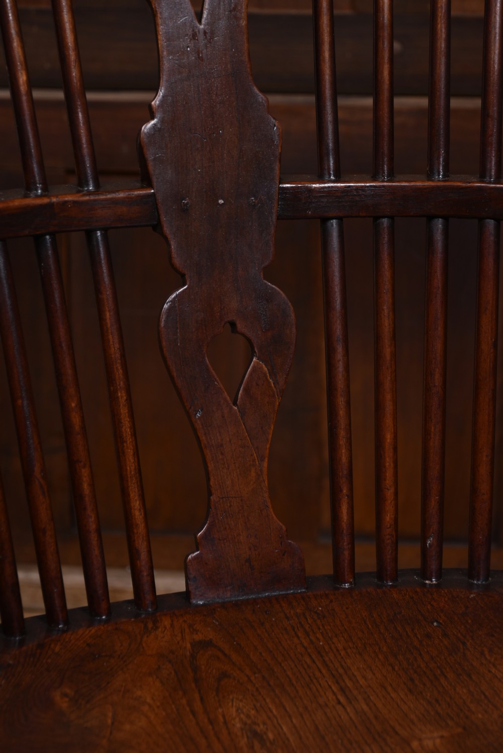 An antique dark brown wooden Windsor armchair featuring a pierced wheel-back splat, spindle backrest, shaped armrests, and a contoured solid elm seat. View V