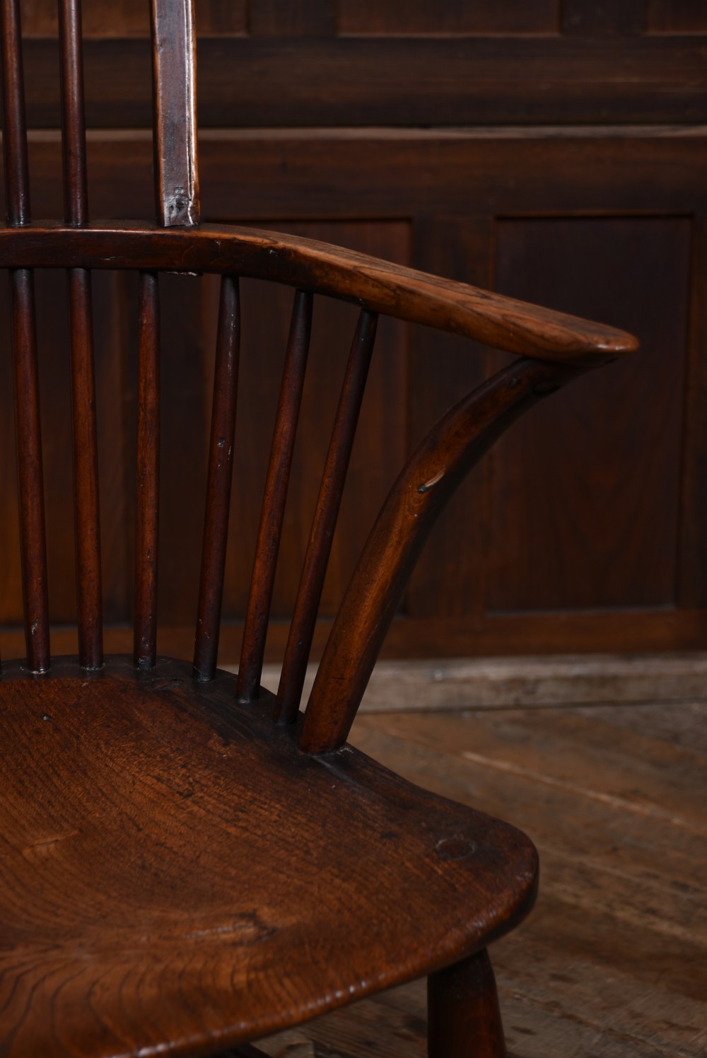 An antique dark brown wooden Windsor armchair featuring a pierced wheel-back splat, spindle backrest, shaped armrests, and a contoured solid elm seat. View VI