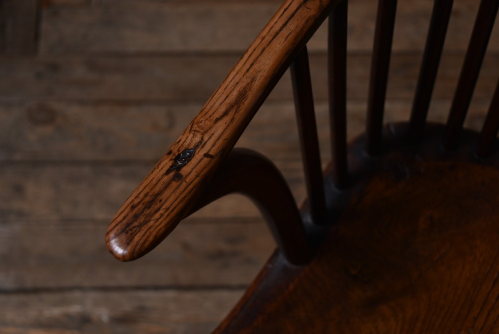 An antique dark brown wooden Windsor armchair featuring a pierced wheel-back splat, spindle backrest, shaped armrests, and a contoured solid elm seat. View XIII