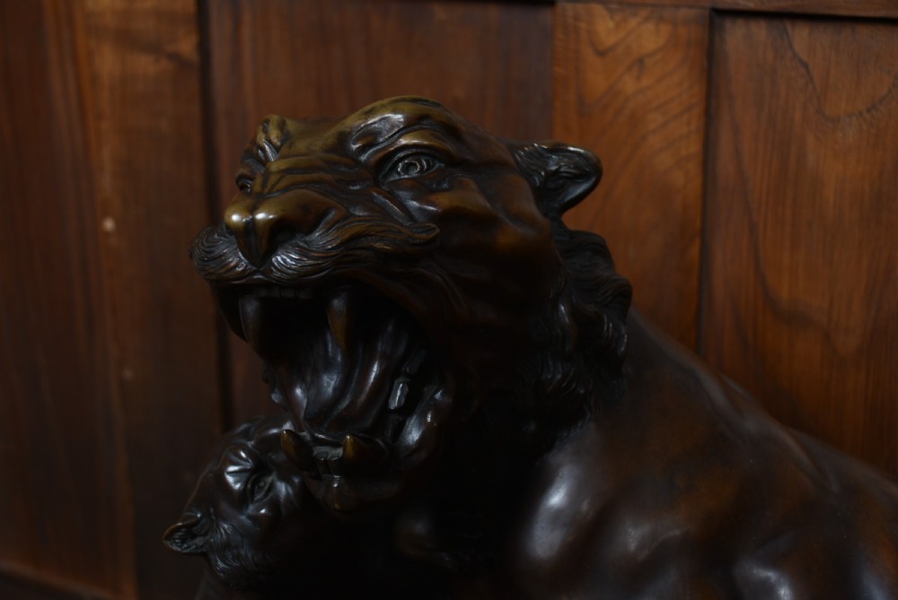A dark patinated bronze sculpture depicting a snarling tigress protecting her two cubs on a textured ground base. View VI