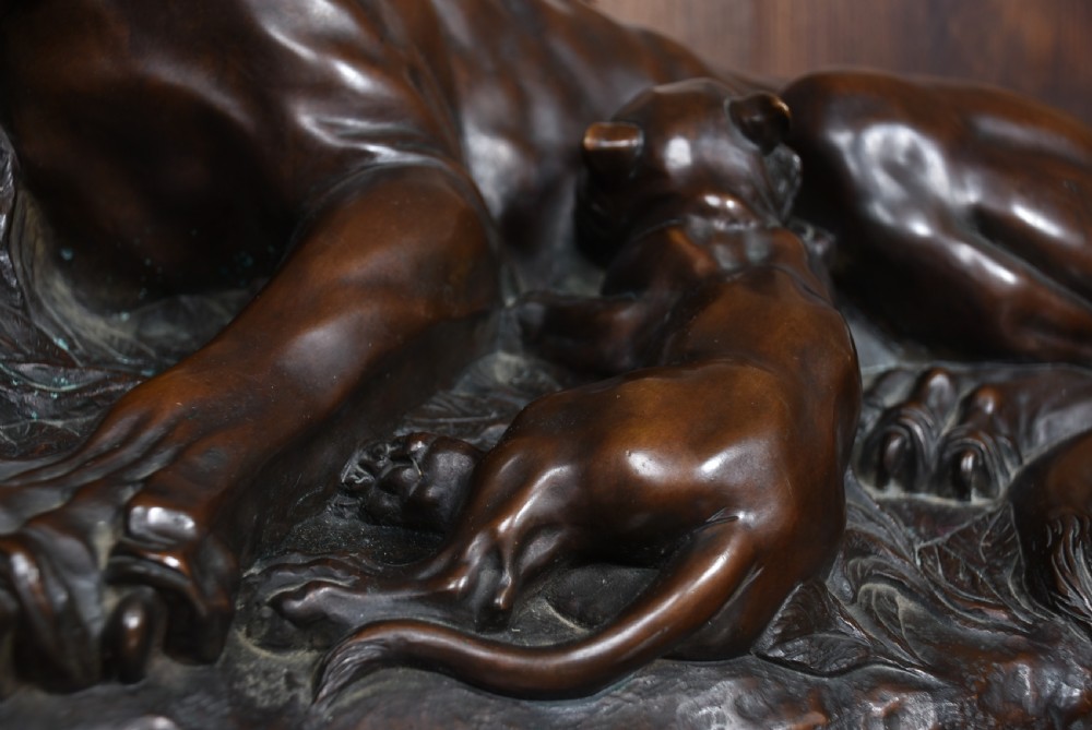 A dark patinated bronze sculpture depicting a snarling tigress protecting her two cubs on a textured ground base. View X