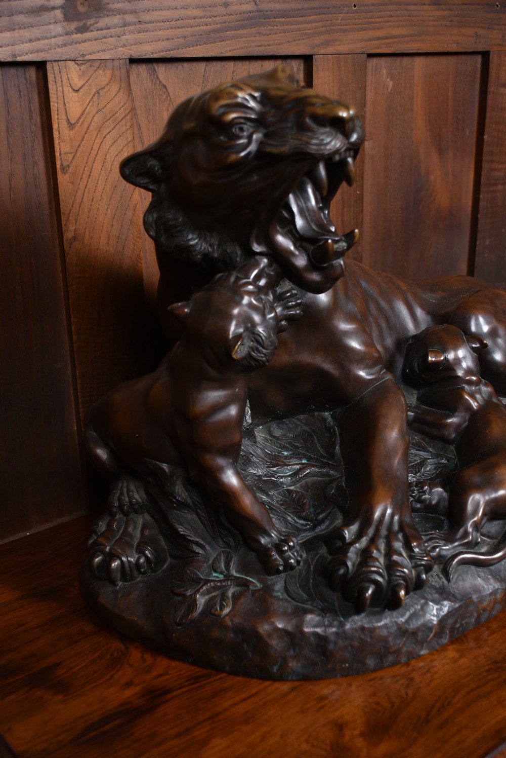 A dark patinated bronze sculpture depicting a snarling tigress protecting her two cubs on a textured ground base. View XII