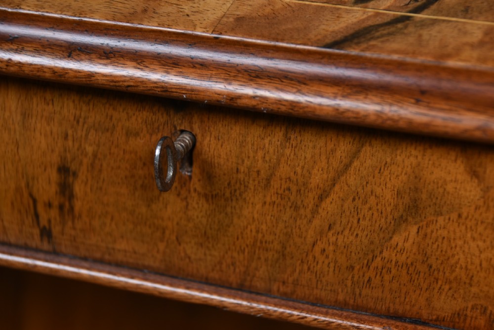 A Victorian burr walnut Davenport desk featuring a slanted brown leather writing top, carved front support columns, side drawers, and castors. View VI