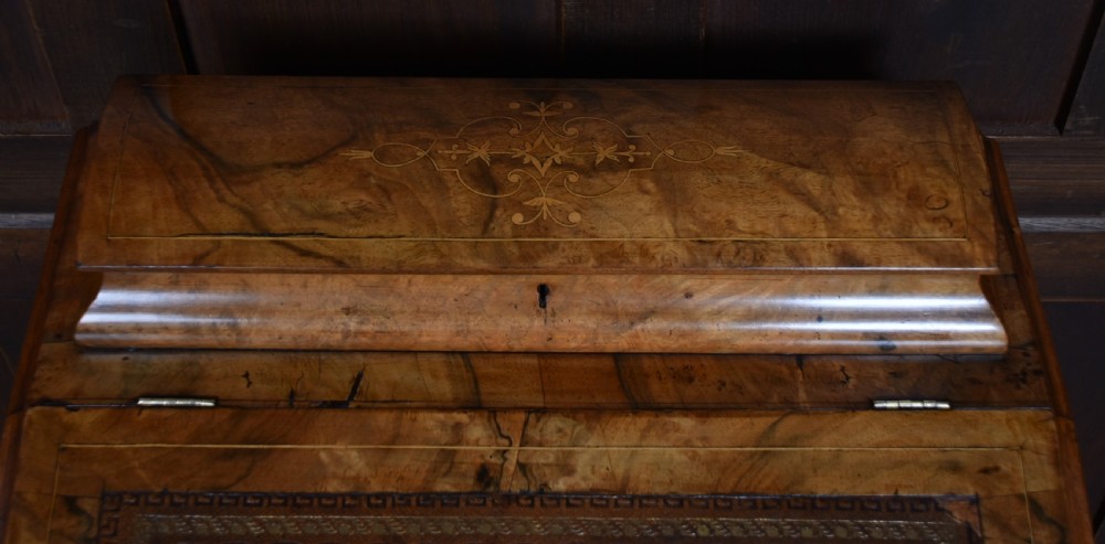 A Victorian burr walnut Davenport desk featuring a slanted brown leather writing top, carved front support columns, side drawers, and castors. View XVII