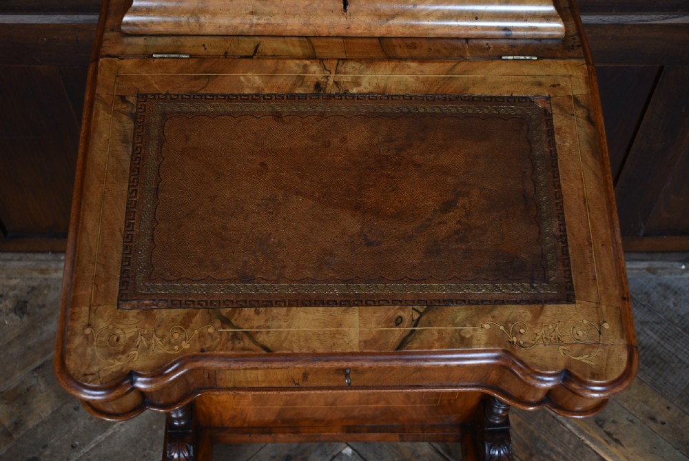 A Victorian burr walnut Davenport desk featuring a slanted brown leather writing top, carved front support columns, side drawers, and castors. View XVIII