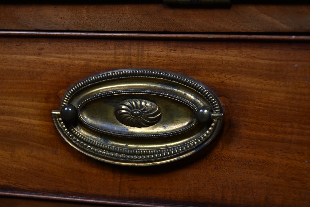 An antique Georgian mahogany slant-front writing bureau featuring four graduated drawers with brass handles and central oval marquetry inlay on the fall flap. View VI