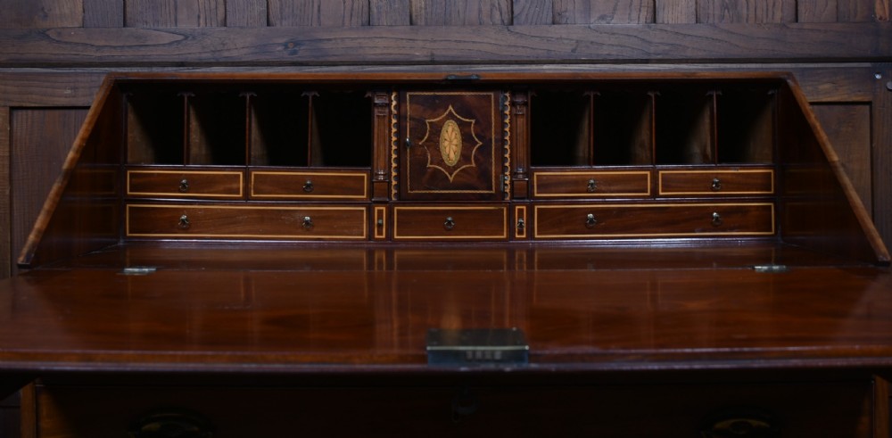An antique Georgian mahogany slant-front writing bureau featuring four graduated drawers with brass handles and central oval marquetry inlay on the fall flap. View VIII