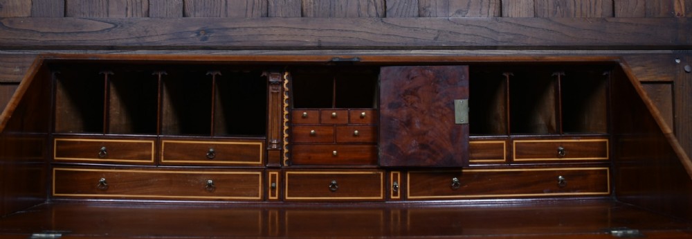 An antique Georgian mahogany slant-front writing bureau featuring four graduated drawers with brass handles and central oval marquetry inlay on the fall flap. View XI