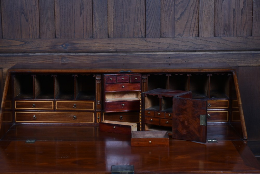 An antique Georgian mahogany slant-front writing bureau featuring four graduated drawers with brass handles and central oval marquetry inlay on the fall flap. View XV