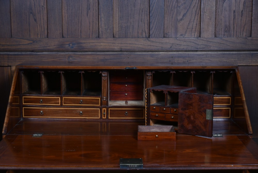 An antique Georgian mahogany slant-front writing bureau featuring four graduated drawers with brass handles and central oval marquetry inlay on the fall flap. View XVI