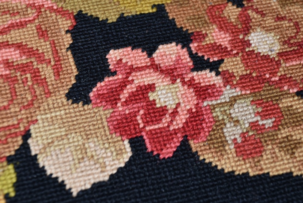 A low Victorian walnut centre stool with carved cabriole legs on brass castors, upholstered in a black floral needlepoint top with green velvet sides. View VI