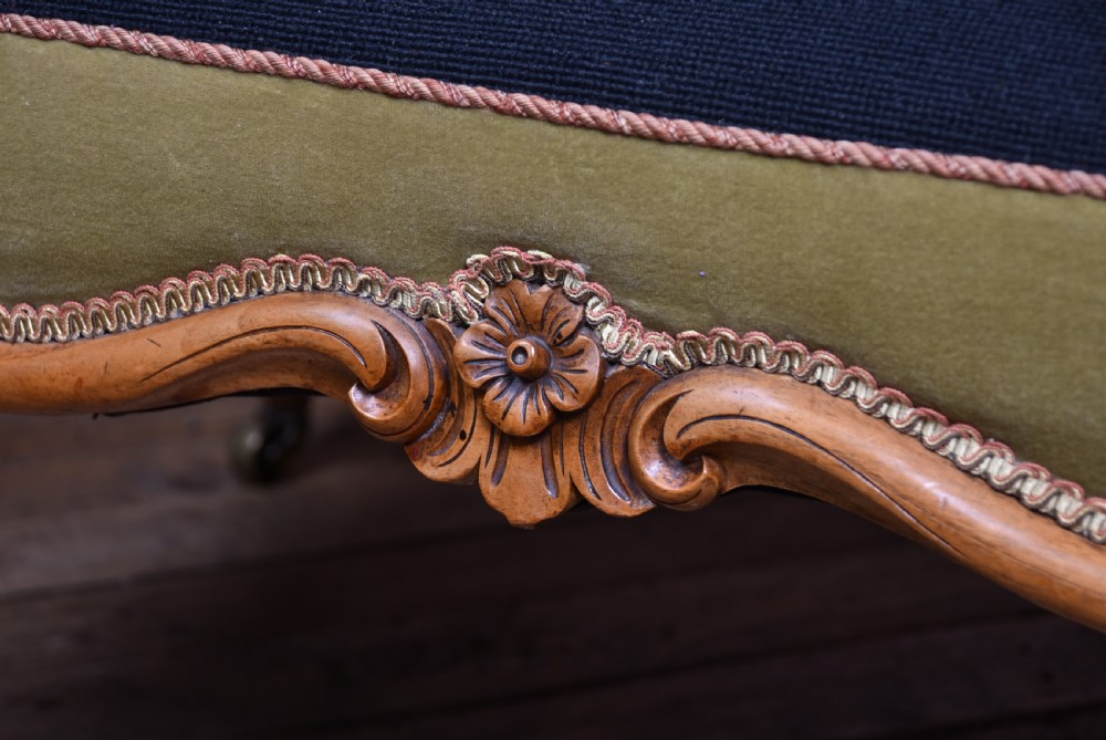 A low Victorian walnut centre stool with carved cabriole legs on brass castors, upholstered in a black floral needlepoint top with green velvet sides. View XI