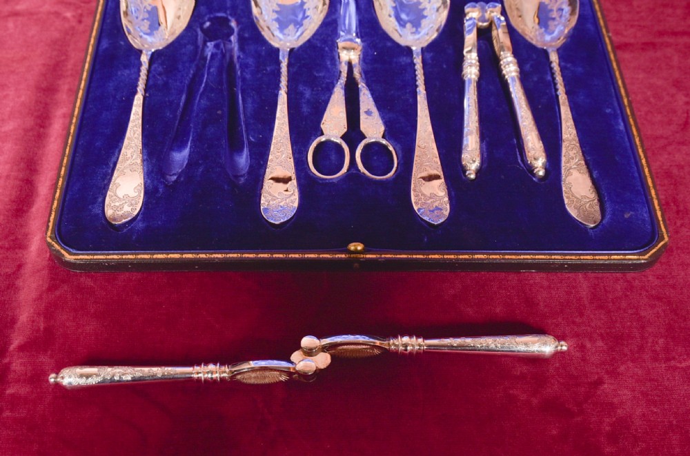 An antique cased silver-plate fruit and nut serving set with four engraved spoons, two nutcrackers, and grape shears set in a cobalt blue velvet lining. View X