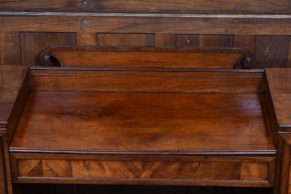 A Regency flame mahogany pedestal sideboard featuring side cupboard pedestals with spiral rope-twist columns, a central drawer section, brass ring handles, and a low rear gallery. View VII