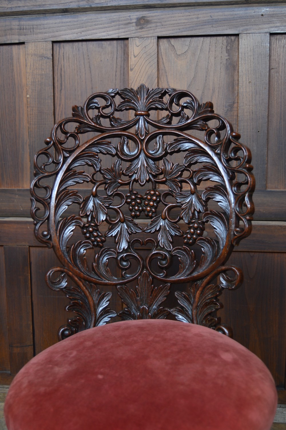 An antique Anglo-Burmese carved padouk wood music chair featuring an intricate openwork back, round crimson velvet upholstered seat, and carved legs. View V
