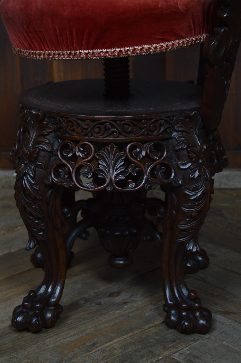 An antique Anglo-Burmese carved padouk wood music chair featuring an intricate openwork back, round crimson velvet upholstered seat, and carved legs. View XII