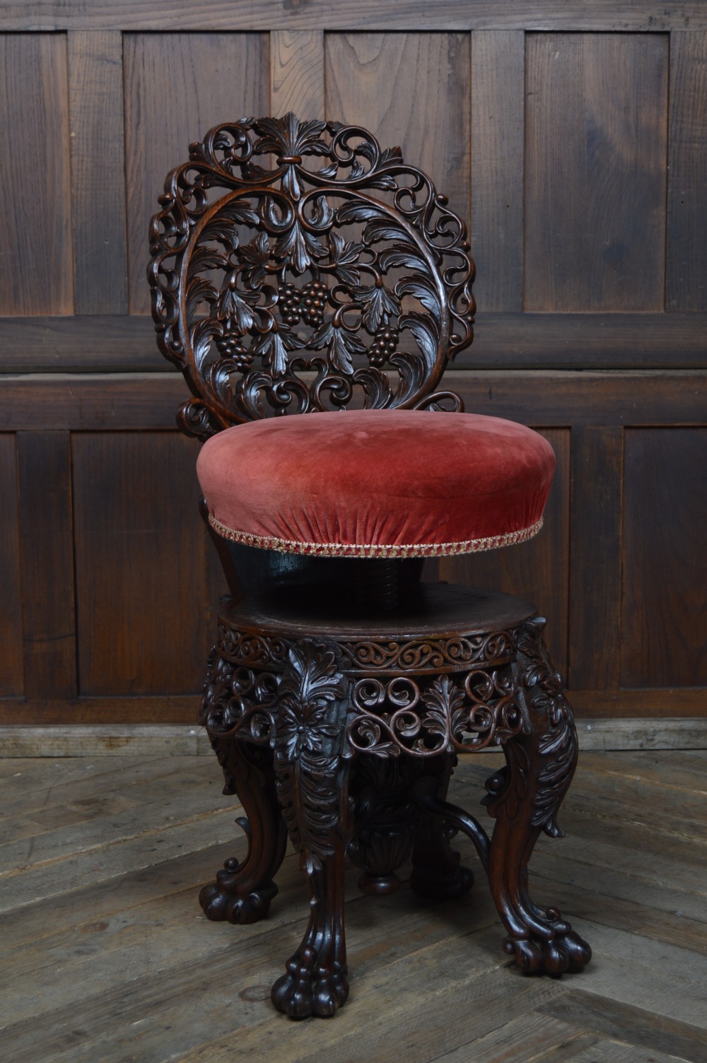 An antique Anglo-Burmese carved padouk wood music chair featuring an intricate openwork back, round crimson velvet upholstered seat, and carved legs. View XIII
