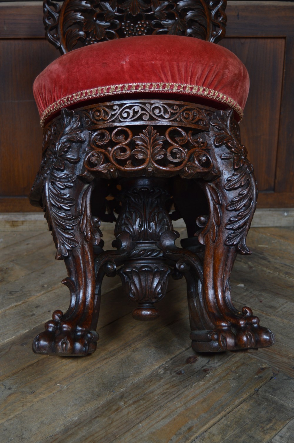 An antique Anglo-Burmese carved padouk wood music chair featuring an intricate openwork back, round crimson velvet upholstered seat, and carved legs. View XIV
