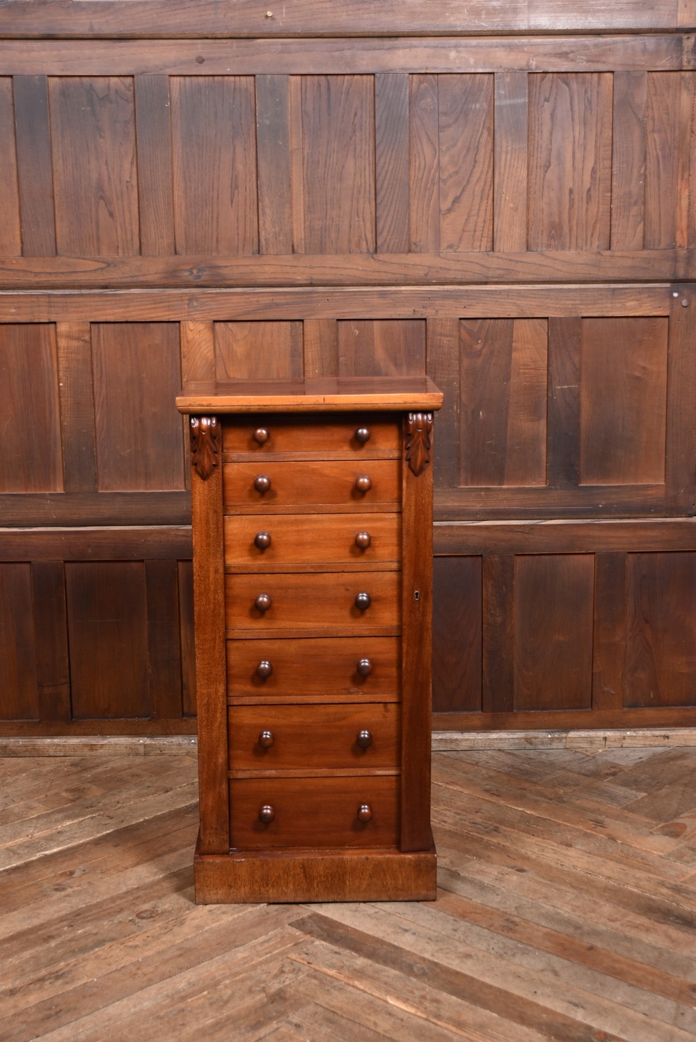 A tall Victorian mahogany Wellington chest featuring seven graduated drawers with turned knobs and a carved side locking pilaster. View V