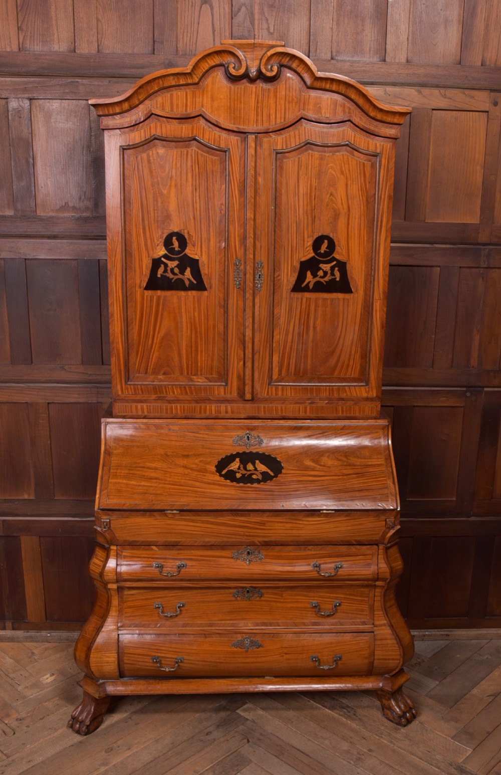 An 18th-century Dutch walnut bombe bureau bookcase featuring inlaid bird motifs, a sloping drop-front desk, shaped drawers, and carved claw feet.