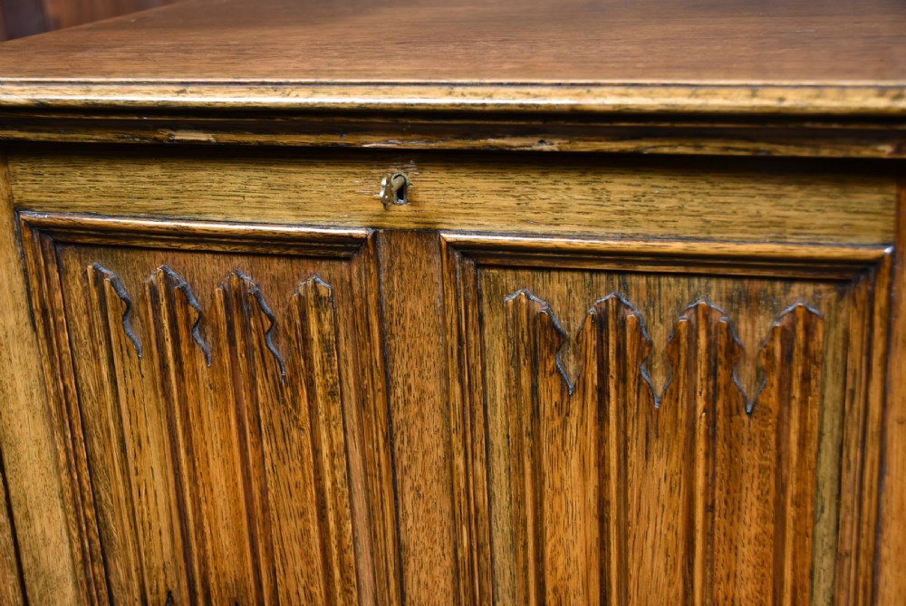 An Edwardian oak writing bureau featuring carved linenfold panel doors, a drawer with brass drop handles, and turned legs. View III