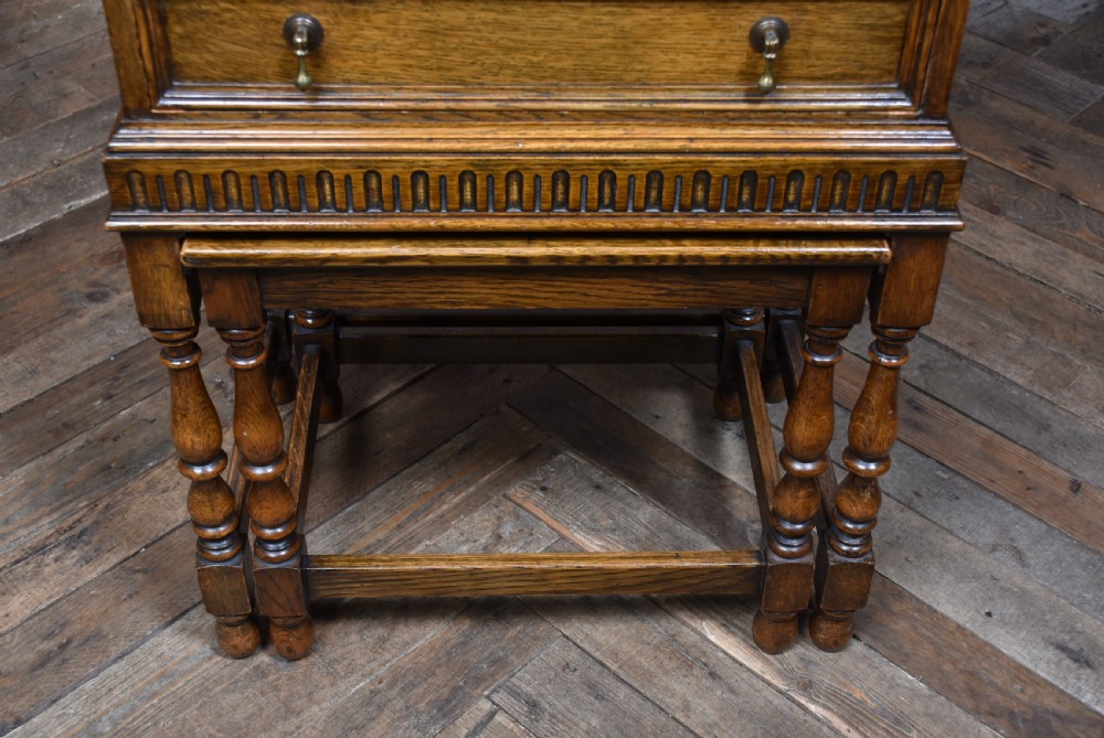 An Edwardian oak writing bureau featuring carved linenfold panel doors, a drawer with brass drop handles, and turned legs. View VII