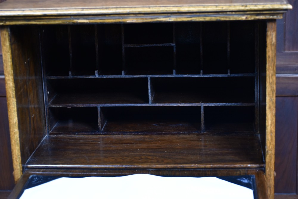 An Edwardian oak writing bureau featuring carved linenfold panel doors, a drawer with brass drop handles, and turned legs. View XI