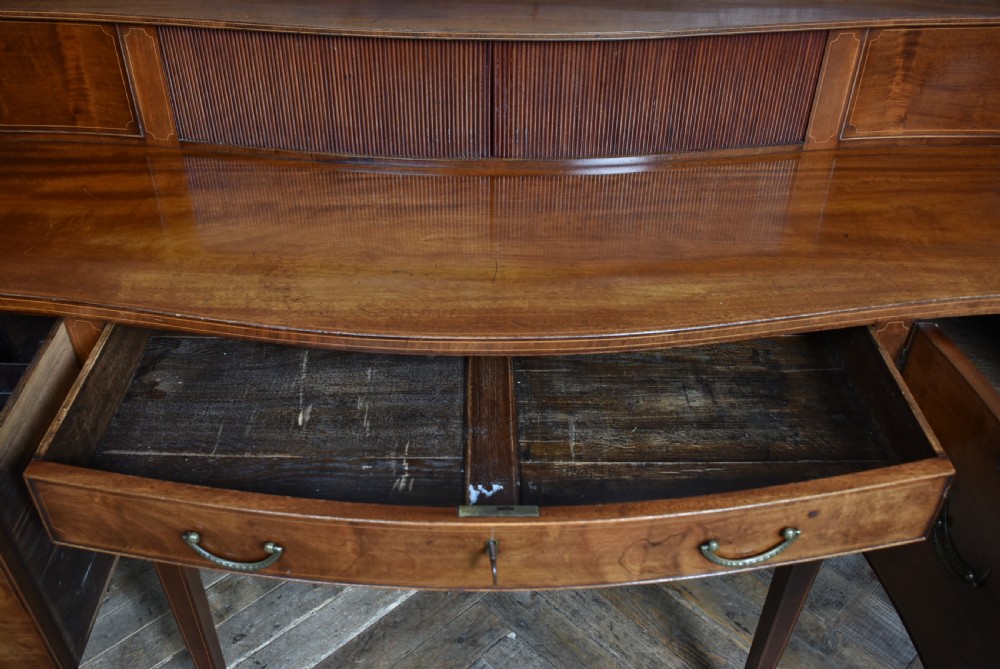 An Edwardian mahogany sideboard featuring satinwood string inlay, a curved central drawer, flanking cupboard doors, a raised superstructure, and square tapered legs. View VIII