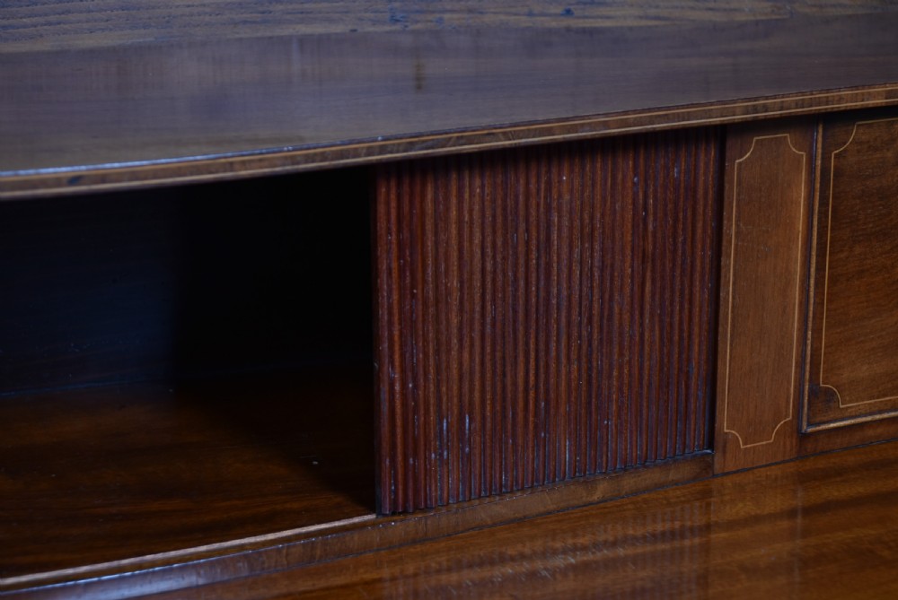 An Edwardian mahogany sideboard featuring satinwood string inlay, a curved central drawer, flanking cupboard doors, a raised superstructure, and square tapered legs. View XI