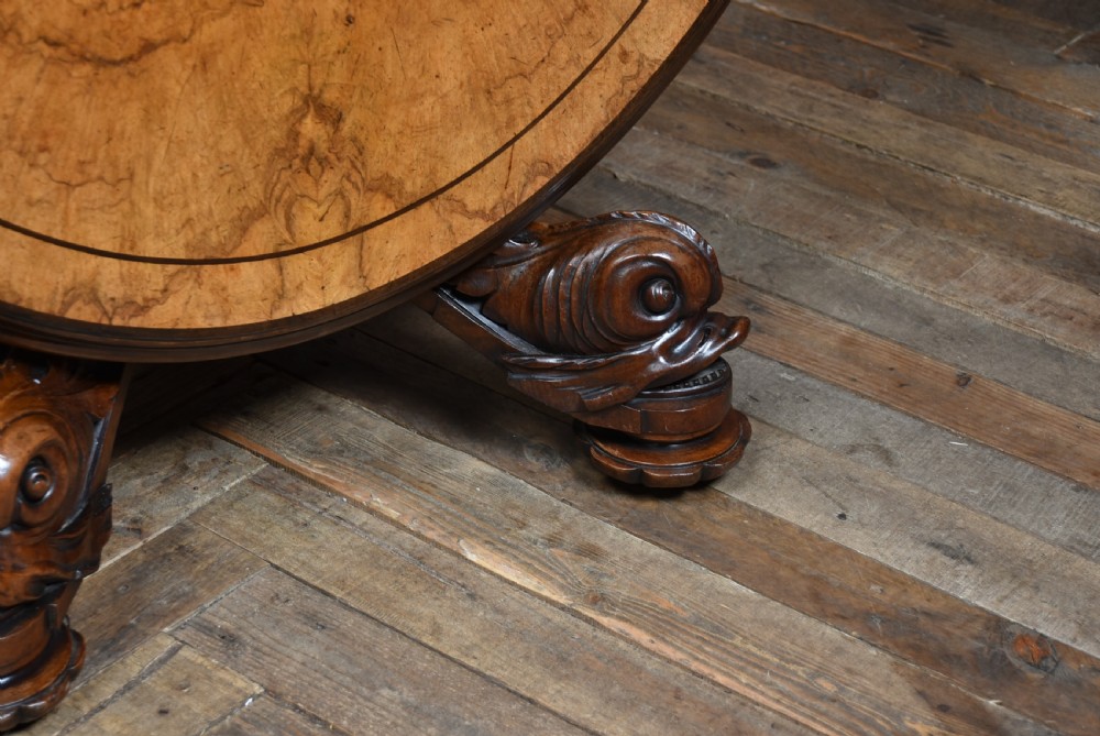 A round Victorian burr walnut snap-top table featuring inlaid border details and a carved quadruped pedestal base with scrolled feet. View V