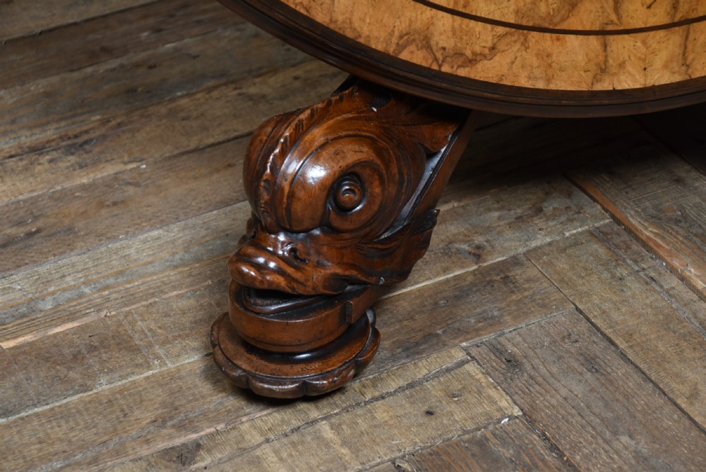 A round Victorian burr walnut snap-top table featuring inlaid border details and a carved quadruped pedestal base with scrolled feet. View VI